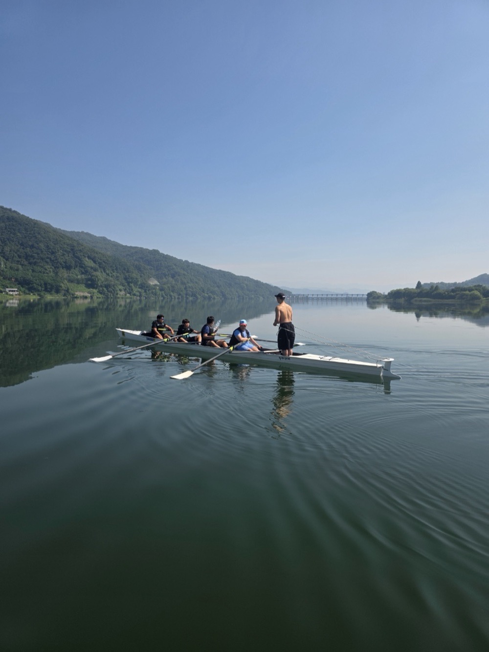 A coach guiding a rowing crew on a calm lake